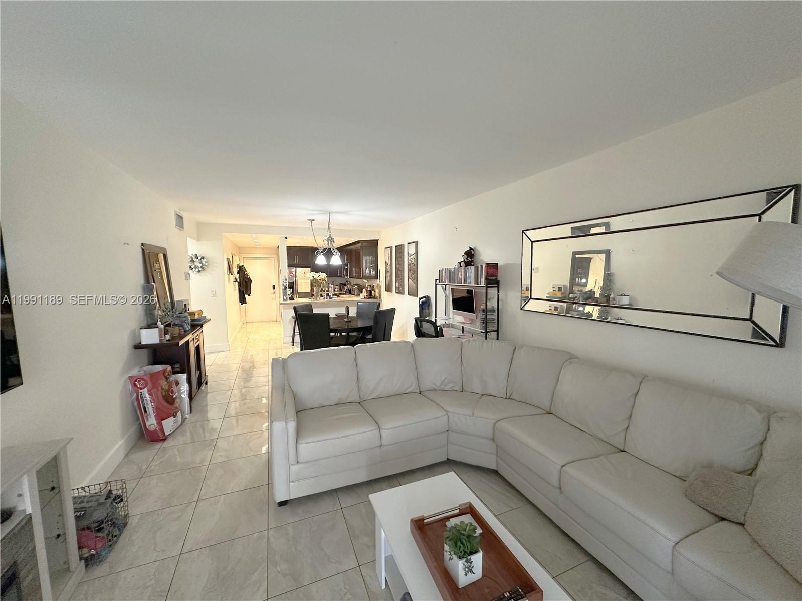 A white sectional sofa sits in a living room with tile floors and a mirror — 450 Paradise Isle Blvd # 102, Hallandale Beach FL 33009, HALLANDALE BEACH, FL