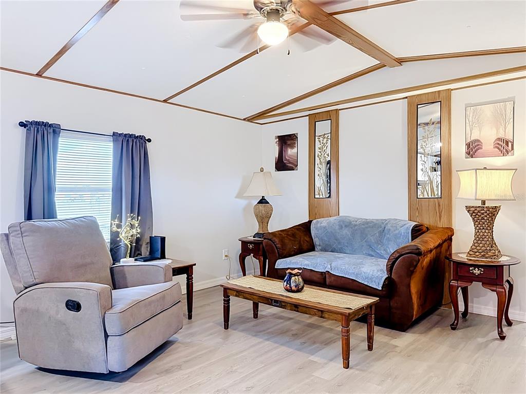 A living room features a recliner, a brown sofa, wood-trimmed ceilings, and light-colored flooring — 1400 NW 12TH LANE, LAKE PANASOFFKEE, FL