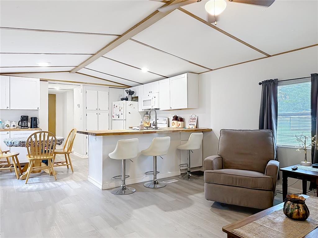 A kitchen with white cabinets and a breakfast bar overlooks a living area with flooring — 1400 NW 12TH LANE, LAKE PANASOFFKEE, FL
