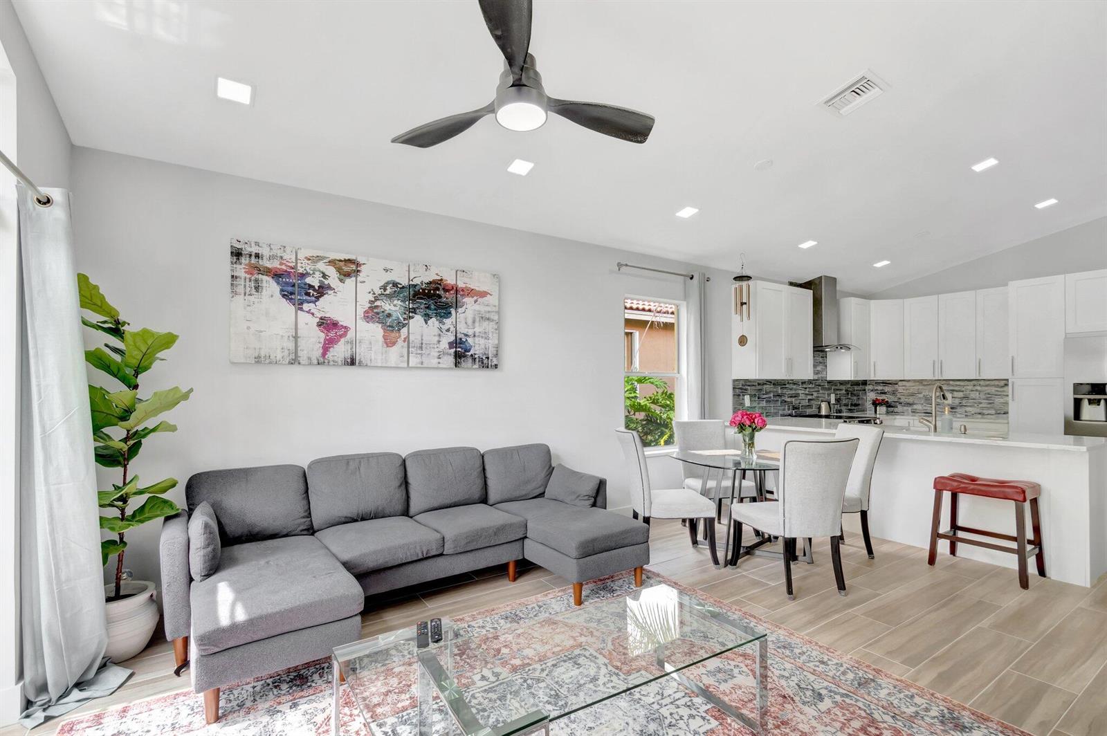 A modern open-concept living room and kitchen featuring a gray sectional sofa and dining area — 9640 Cherry Blossom Court, Boynton Beach FL 33437, BOYNTON BEACH, FL