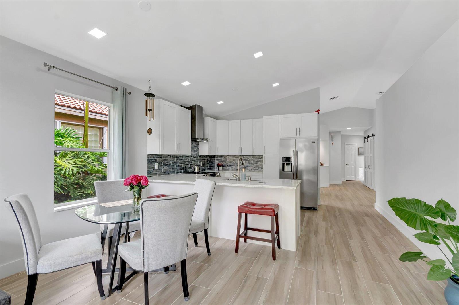 A kitchen and dining area with white cabinets, stainless steel appliances, and light wood flooring — 9640 Cherry Blossom Court, Boynton Beach FL 33437, BOYNTON BEACH, FL