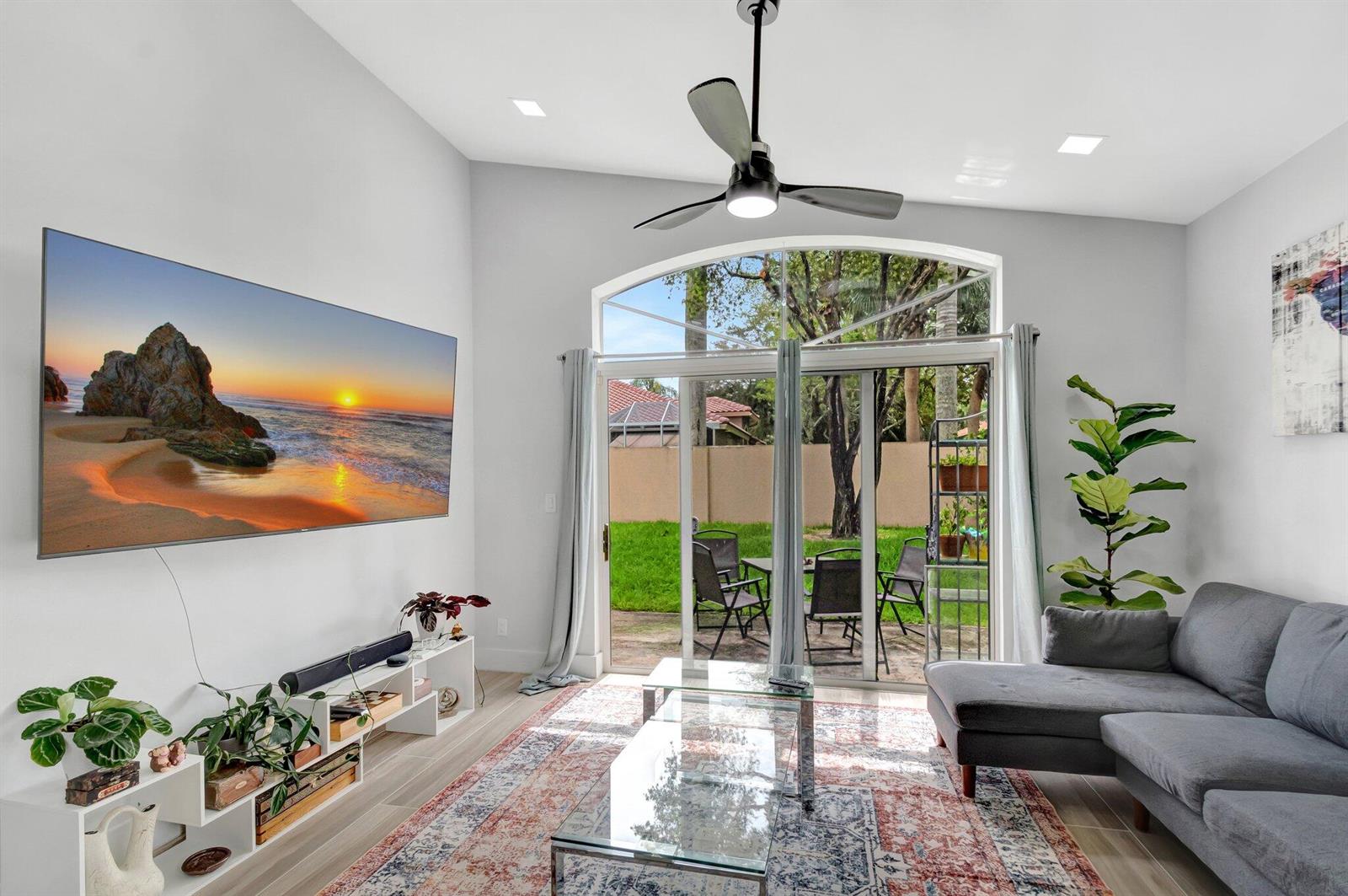 A living room with a large wall-mounted television, gray sectional sofa, and sliding glass doors — 9640 Cherry Blossom Court, Boynton Beach FL 33437, BOYNTON BEACH, FL