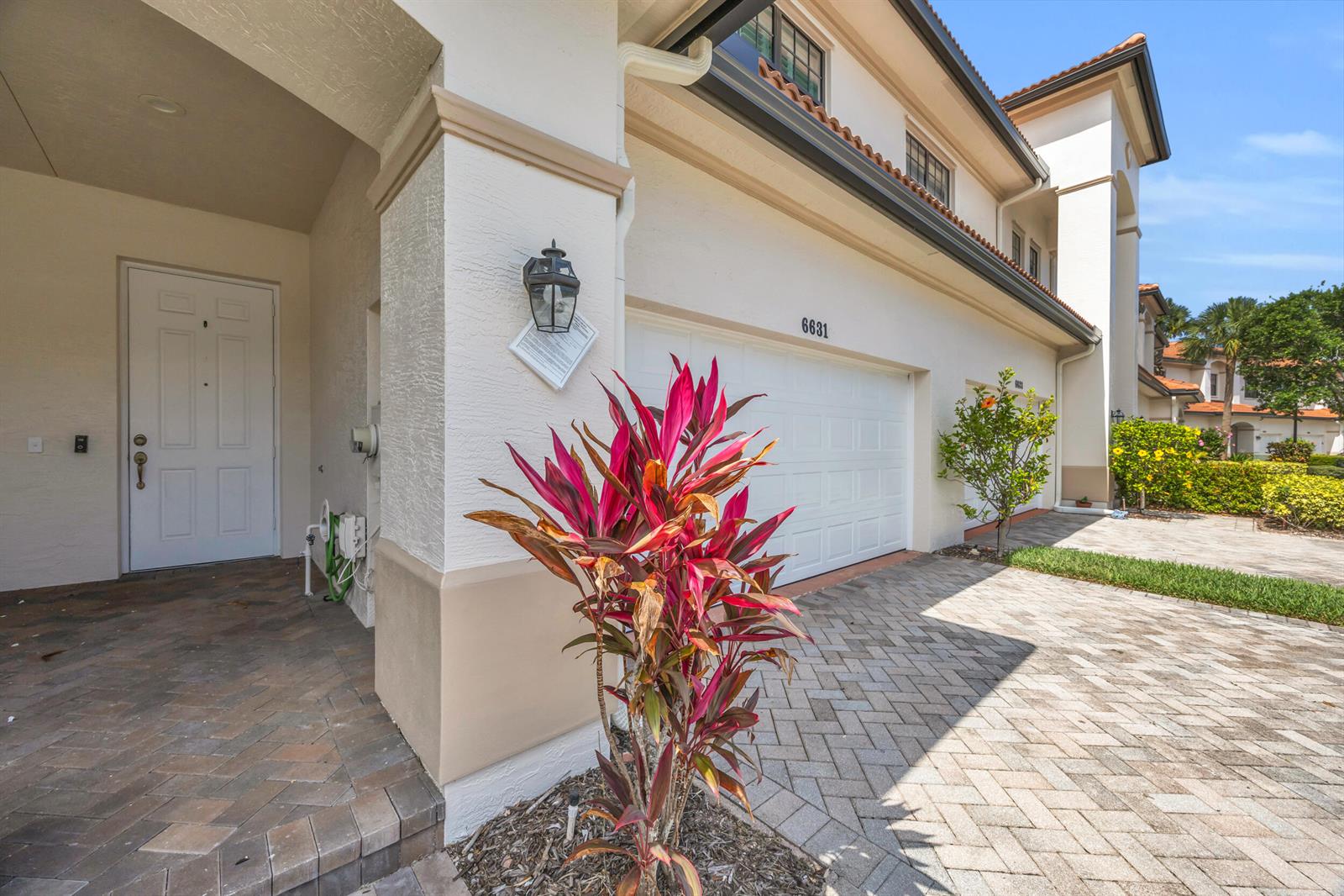 A residential exterior features a white garage, a front door, and a colorful tropical plant — 6631 SE Woodmill Pond Lane, Stuart FL 34997, STUART, FL