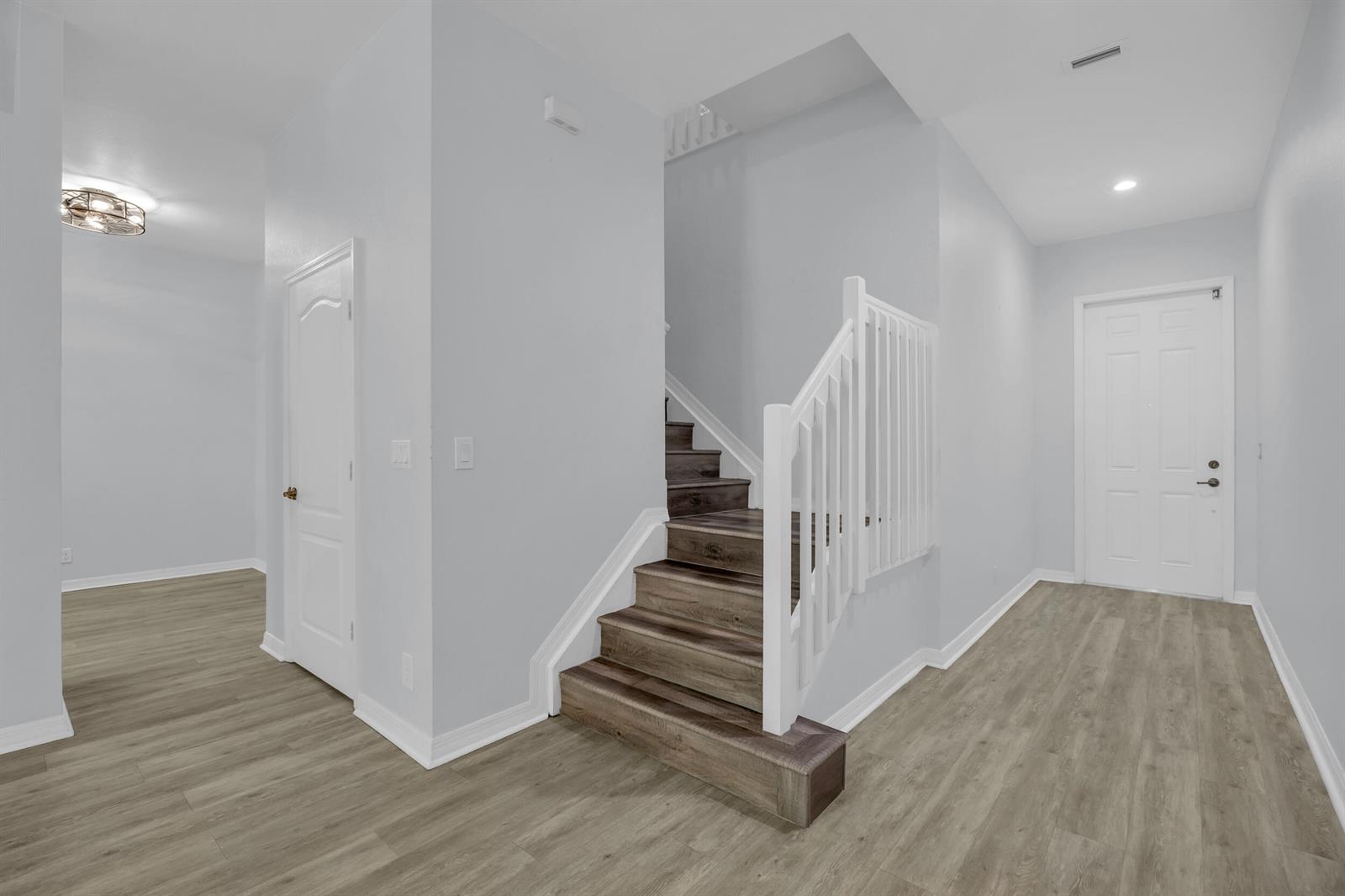 An interior view of a foyer featuring wood-look flooring, a staircase, and a white door — 6631 SE Woodmill Pond Lane, Stuart FL 34997, STUART, FL