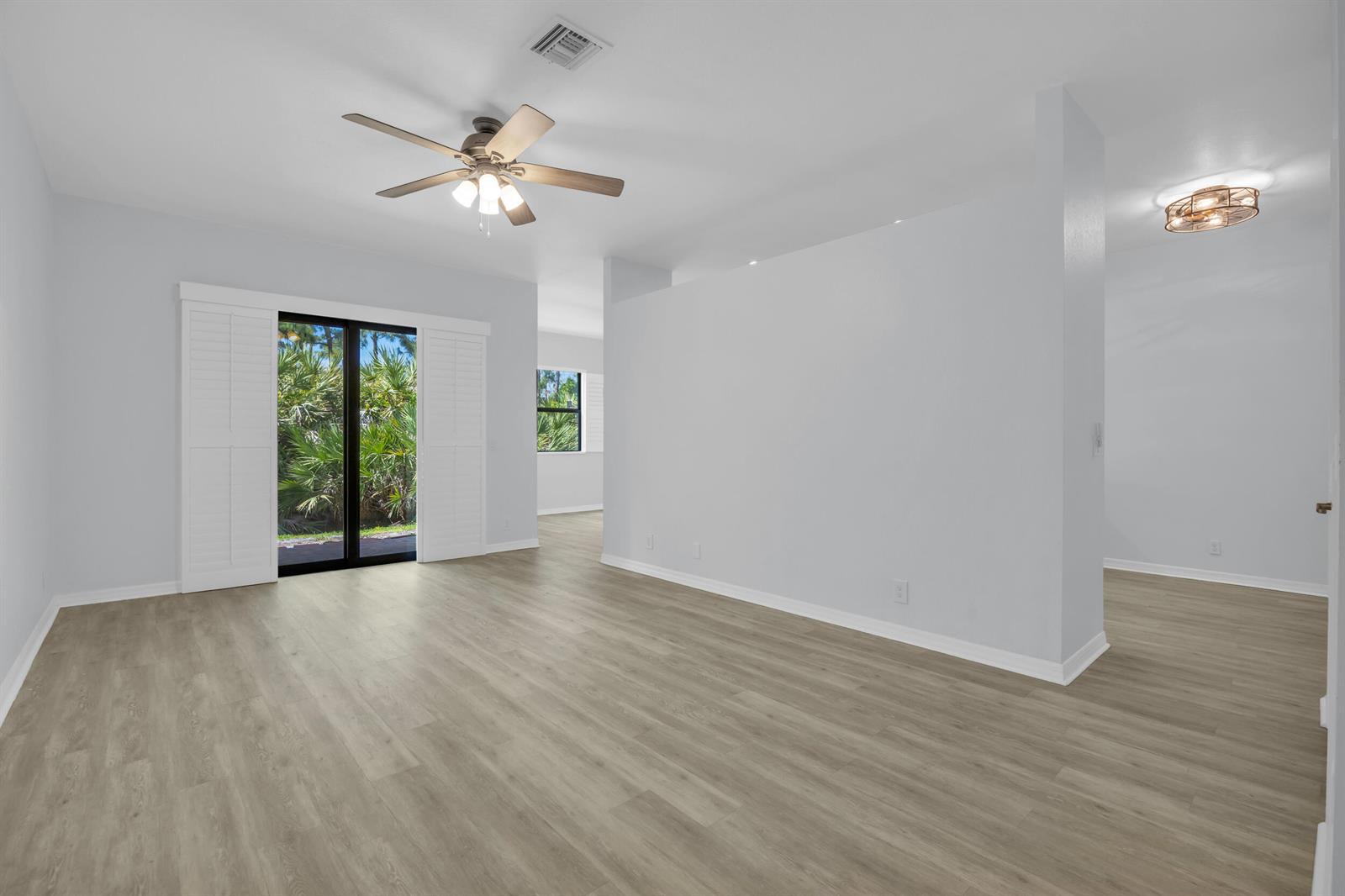 An empty room with light wood-look flooring, a ceiling fan, and sliding glass doors — 6631 SE Woodmill Pond Lane, Stuart FL 34997, STUART, FL