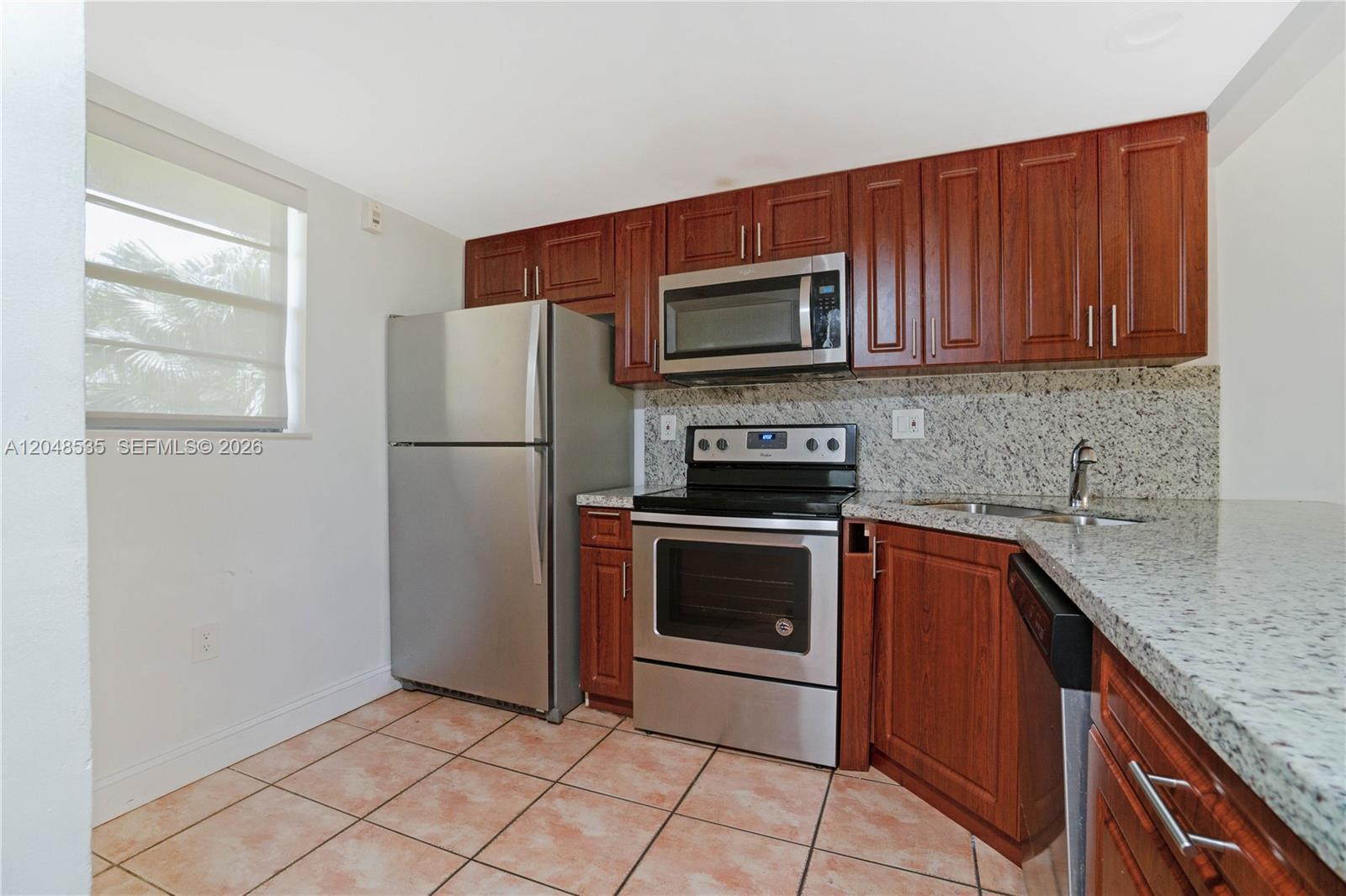 A kitchen features stainless steel appliances, cherry wood cabinets, and granite countertops over tile flooring — 10525 SW 112th Ave # 309, Miami FL 33176, MIAMI, FL