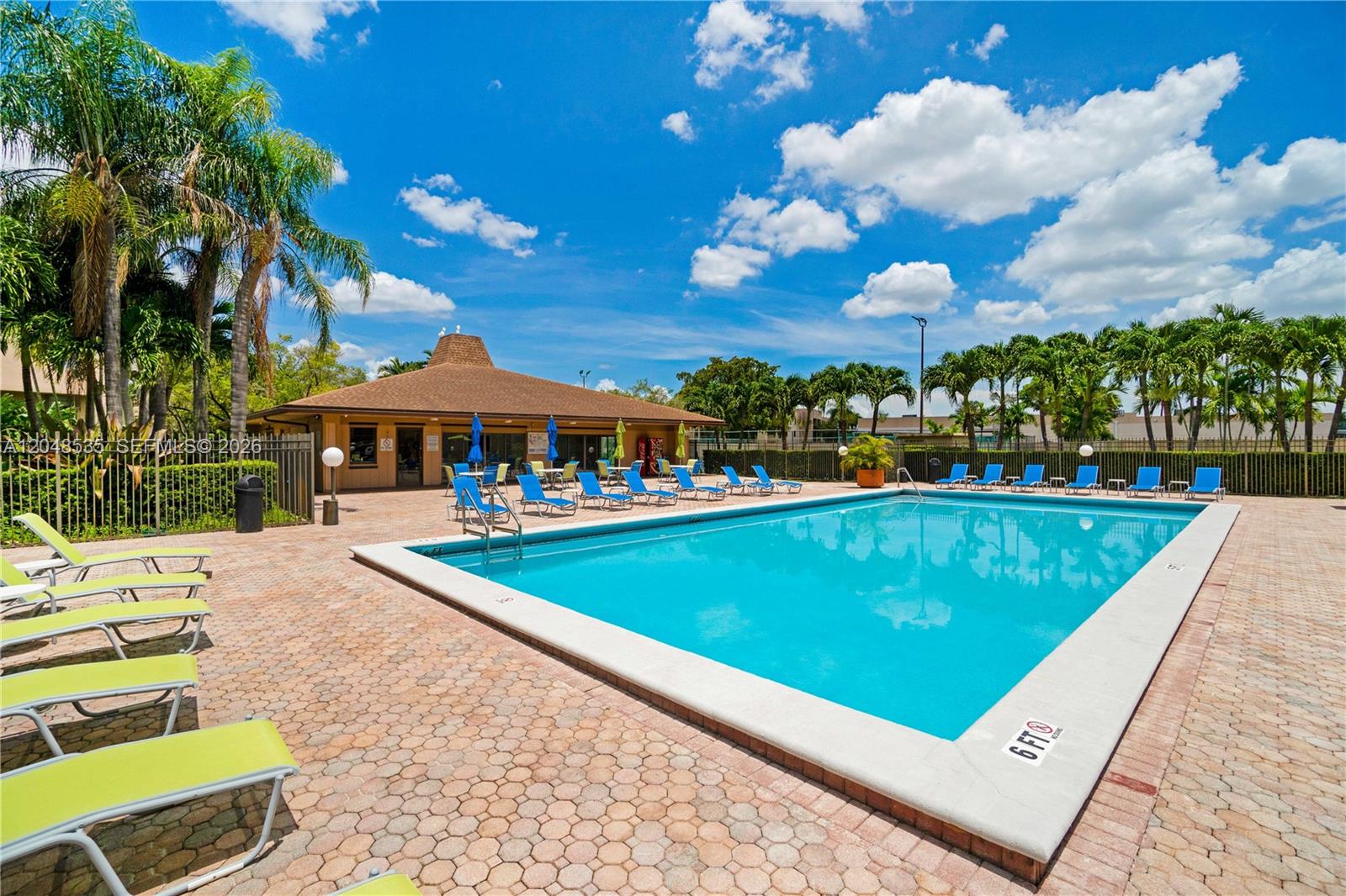 An outdoor swimming pool surrounded by lounge chairs and a clubhouse under a blue sky — 10525 SW 112th Ave # 309, Miami FL 33176, MIAMI, FL
