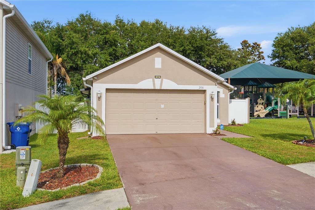 A tan single-story house with a two-car garage and a driveway next to a playground — 2816 MINGO DRIVE, LAND O LAKES, FL