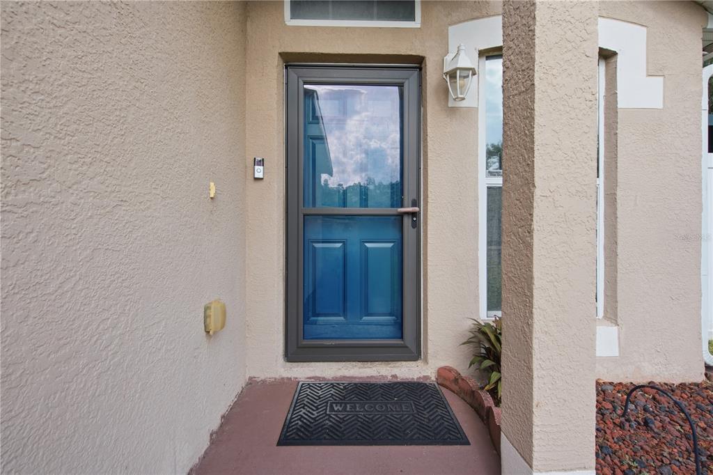 A front entryway features a blue door with a storm door and a welcome mat — 2816 MINGO DRIVE, LAND O LAKES, FL