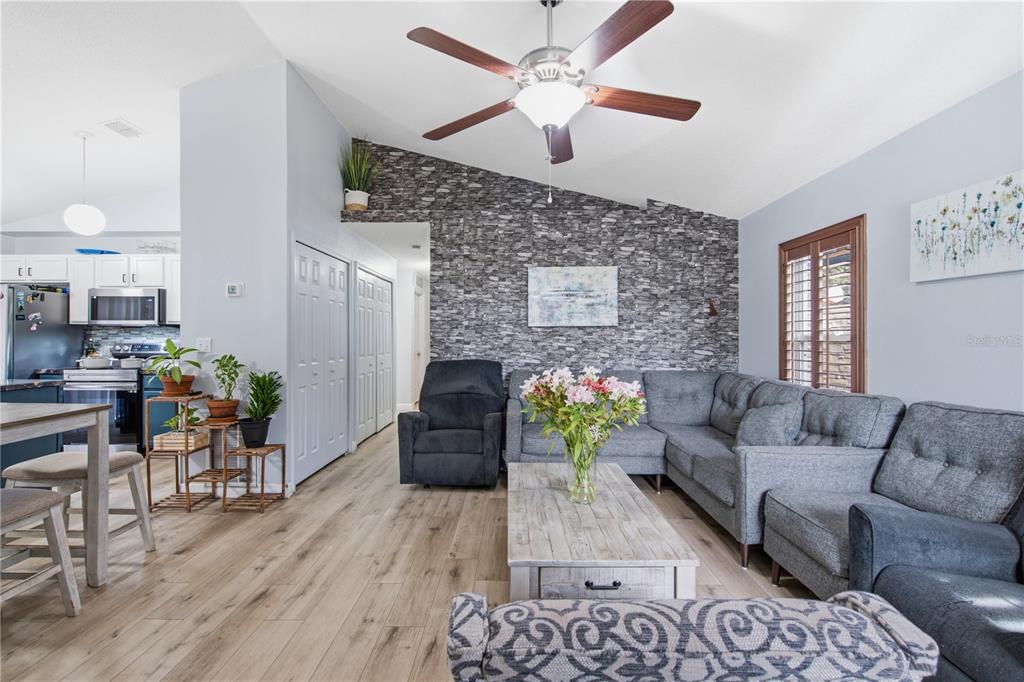 A living room features a stone accent wall, gray sectional sofa, and light wood flooring — 2816 MINGO DRIVE, LAND O LAKES, FL