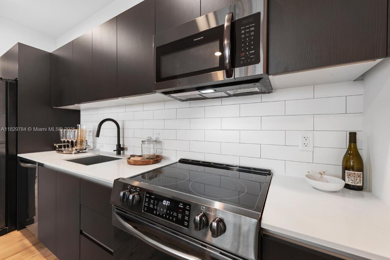 A modern kitchen features dark cabinets, white countertops, a subway tile backsplash, and stainless appliances — 398 NE 5th St # 4207, Miami FL 33132, MIAMI, FL