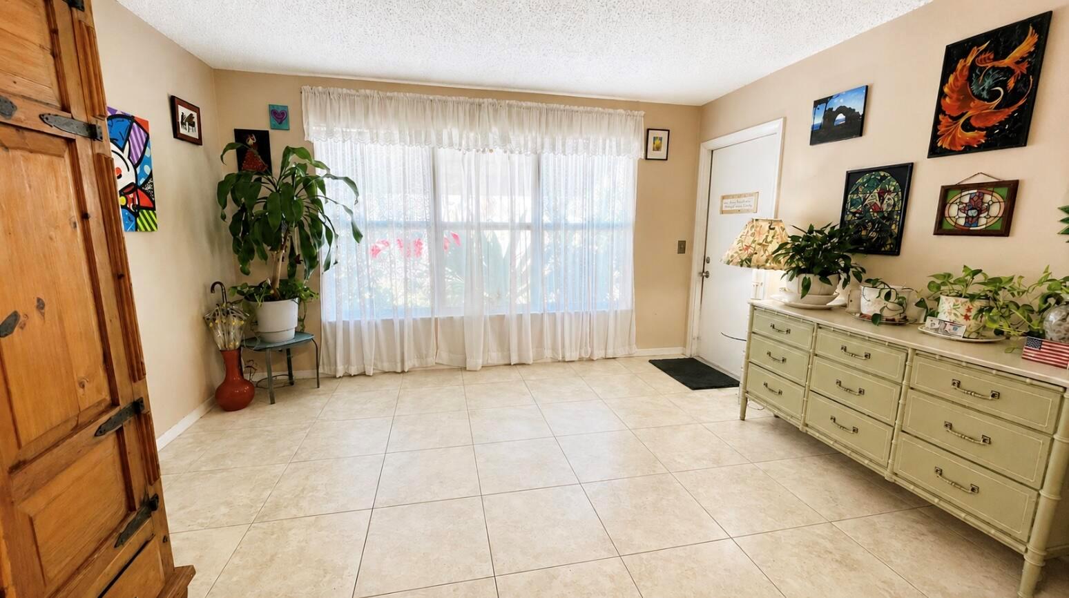 A bright entryway features tile flooring, a large window with white curtains, and a dresser — 910 South Drive # B, Delray Beach FL 33445, DELRAY BEACH, FL