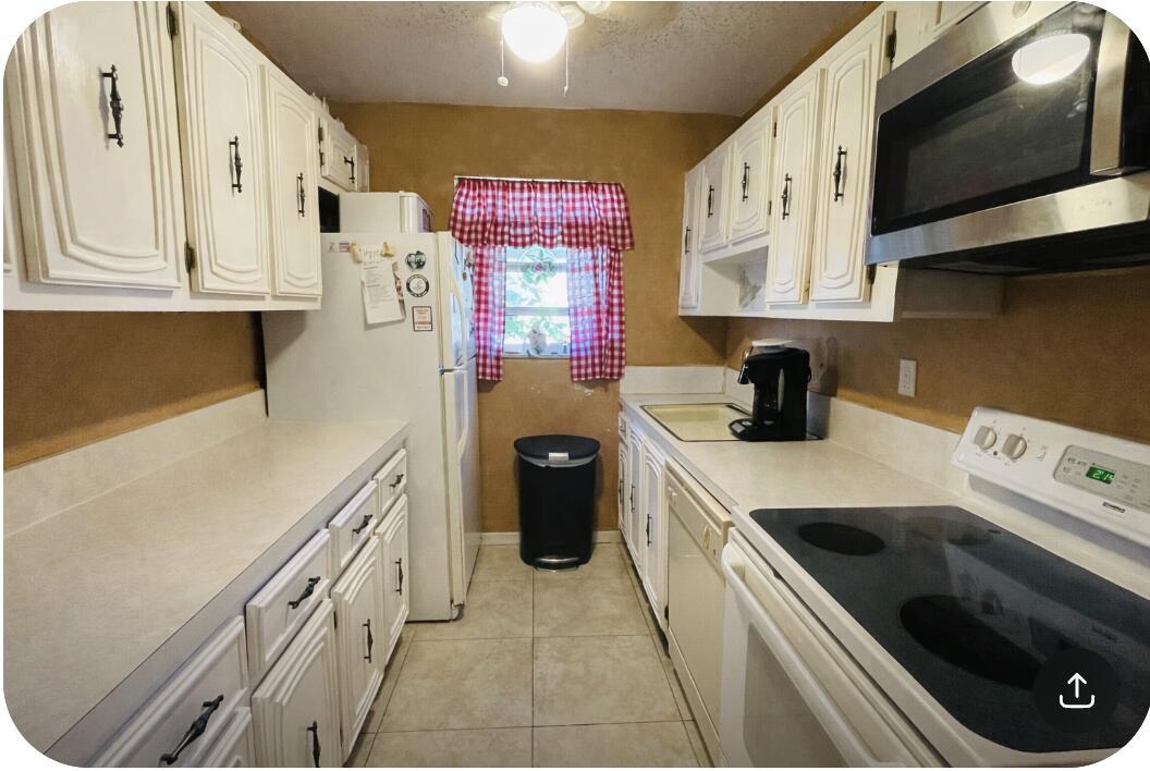 A galley kitchen features white cabinets, laminate countertops, a white refrigerator, and a range — 910 South Drive # B, Delray Beach FL 33445, DELRAY BEACH, FL