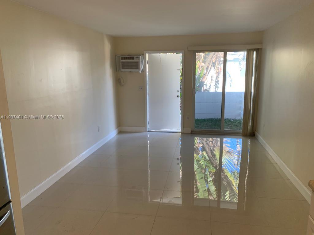 An empty room features light-colored tile flooring, a window air conditioner, and a sliding glass door — 1511 NE 117th St # 2, Miami FL 33161, MIAMI, FL