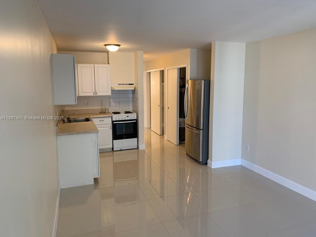 A kitchen features white cabinets, stainless steel appliances, and light-colored tile flooring — 1511 NE 117th St # 2, Miami FL 33161, MIAMI, FL