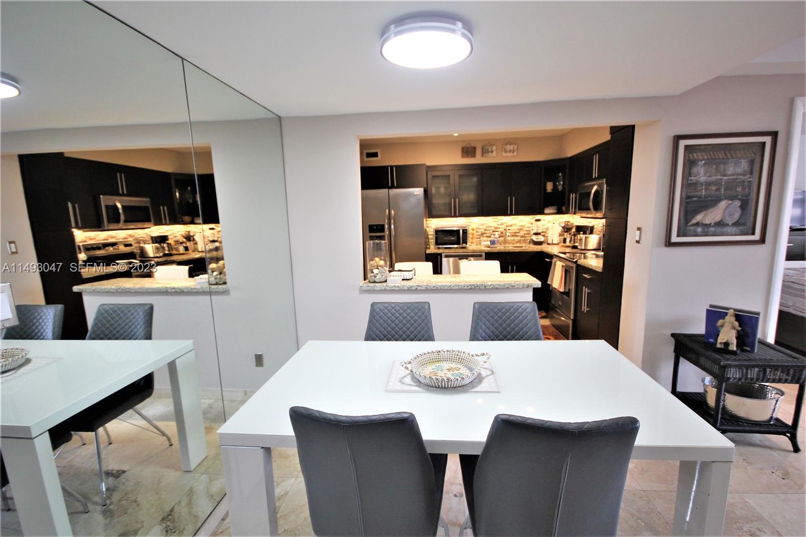 A dining area with a white table and chairs sits before an open-concept kitchen — 5161 Collins Ave # 1610, Miami Beach FL 33140, MIAMI BEACH, FL