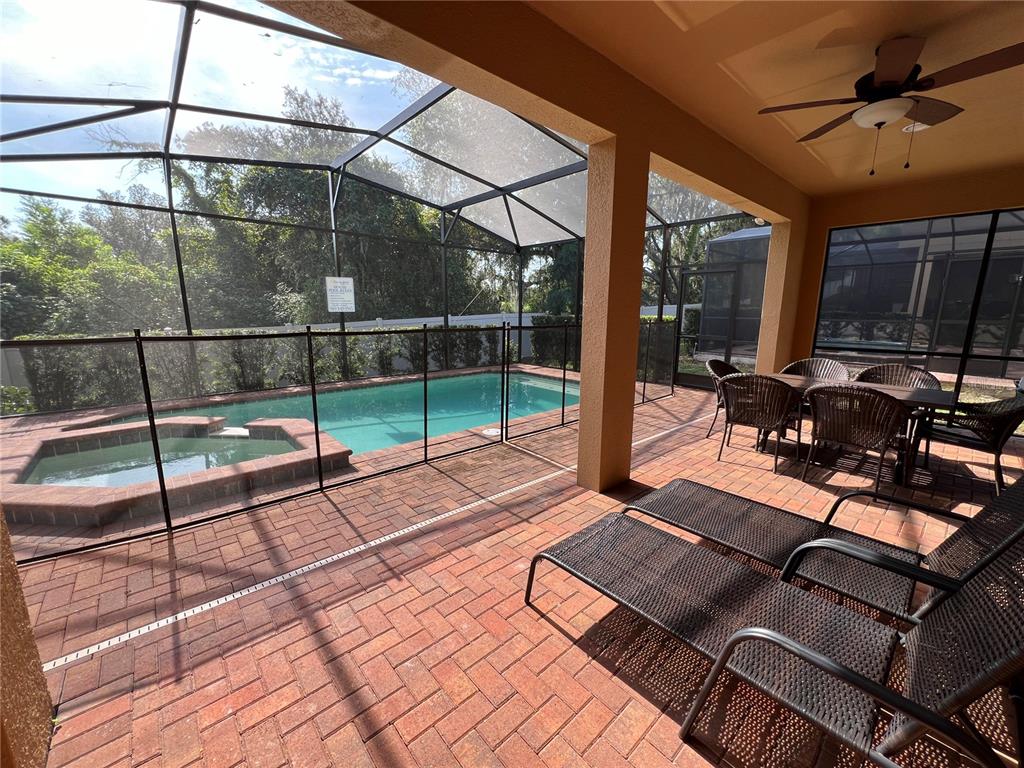 A covered brick patio features a swimming pool, hot tub, and outdoor dining furniture — 1921 NICE COURT, KISSIMMEE, FL