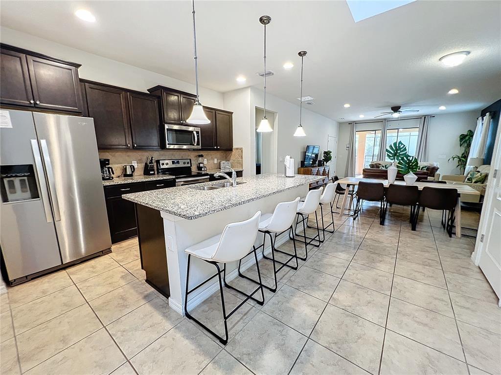 A kitchen with dark cabinets, granite countertops, and a central island with white bar stools — 1921 NICE COURT, KISSIMMEE, FL