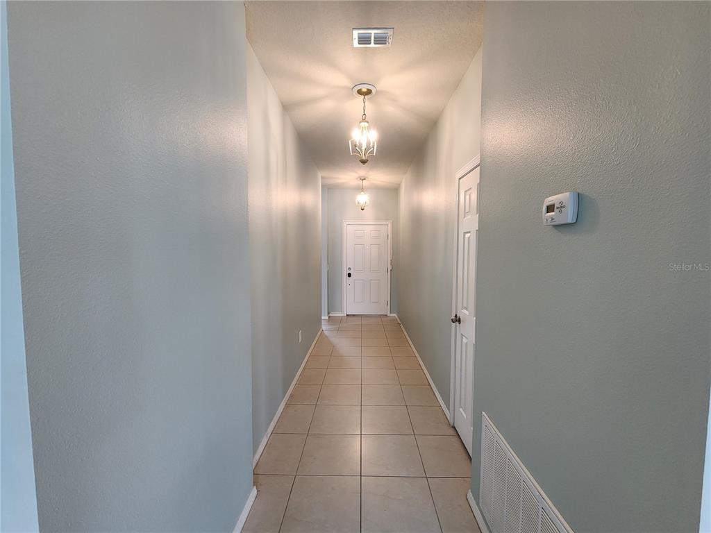 A long hallway with light-colored walls, tile flooring, and two hanging light fixtures — 15734 STONE HOUSE DRIVE, BROOKSVILLE, FL