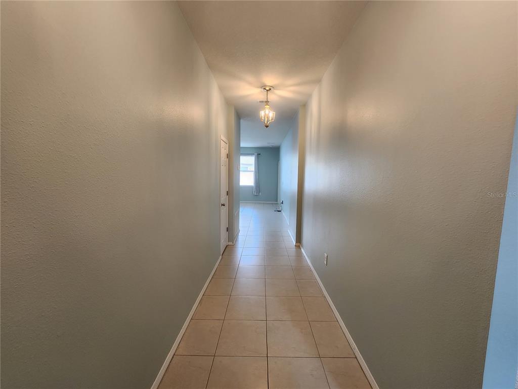A long, tiled hallway leads toward a bright room with a window at the end — 15734 STONE HOUSE DRIVE, BROOKSVILLE, FL