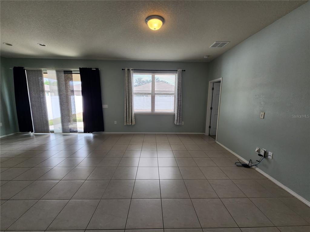 A spacious living area features light-colored tile flooring, pale blue walls, and a sliding glass door — 15734 STONE HOUSE DRIVE, BROOKSVILLE, FL