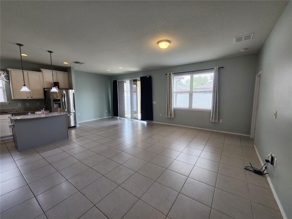 An open-concept living area features light-colored tile flooring, a kitchen island, and sliding glass doors — 15734 STONE HOUSE DRIVE, BROOKSVILLE, FL