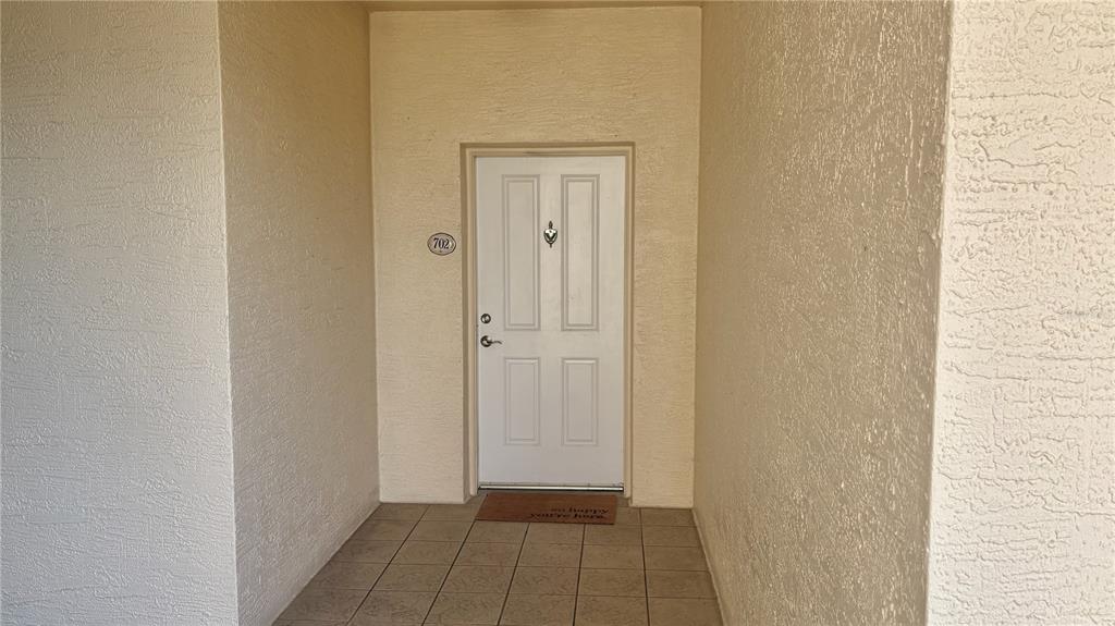 A white front door with a number 702 plaque sits in a tiled entryway — 261 MINORCA BEACH WAY UNIT 702, NEW SMYRNA BEACH, FL