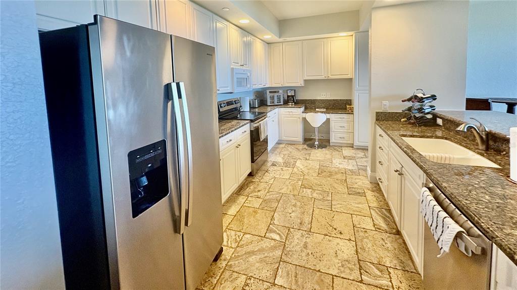 A kitchen features white cabinets, granite countertops, stainless steel appliances, and light-colored stone tile flooring — 261 MINORCA BEACH WAY UNIT 702, NEW SMYRNA BEACH, FL