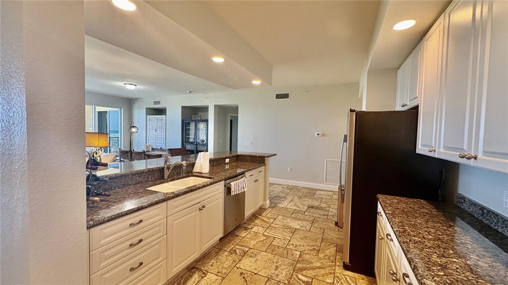 A kitchen features white cabinets, granite countertops, and tile flooring, opening to a dining area — 261 MINORCA BEACH WAY UNIT 702, NEW SMYRNA BEACH, FL