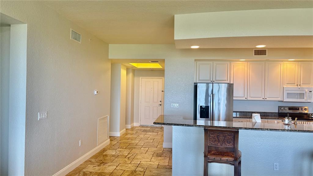 A kitchen with white cabinets and granite countertops overlooks a tiled hallway and entryway — 261 MINORCA BEACH WAY UNIT 702, NEW SMYRNA BEACH, FL