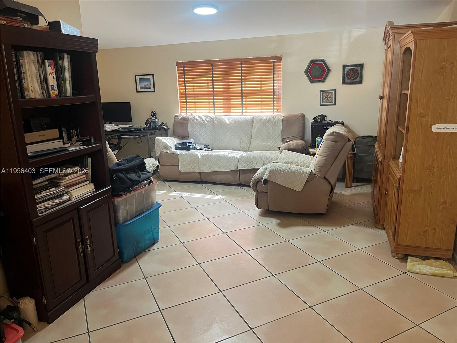 A living room features tile flooring, a beige sofa and recliner, and wooden furniture — 9026 SW 34 ST, Miami FL 33165, MIAMI, FL