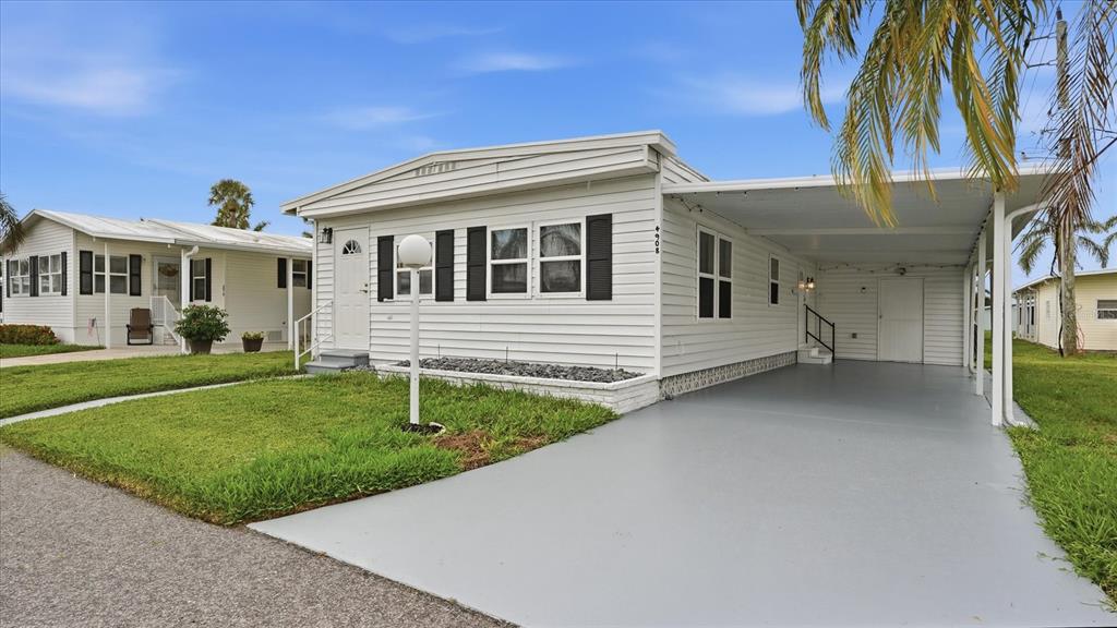 A white single-story manufactured home features black shutters, a gray carport, and a grassy lawn — 4908 5TH A STREET E, BRADENTON, FL
