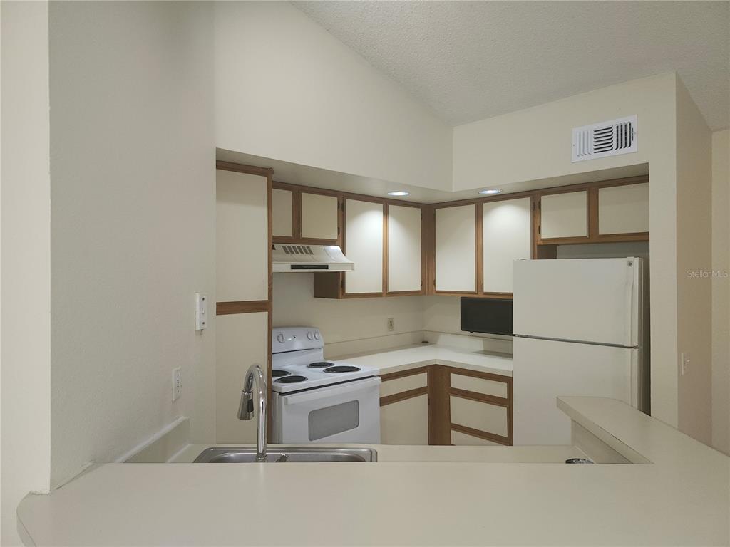 A kitchen with white appliances, wooden cabinets, and a breakfast bar overlooking the sink — 4518 COMMANDER DRIVE UNIT 1934, ORLANDO, FL