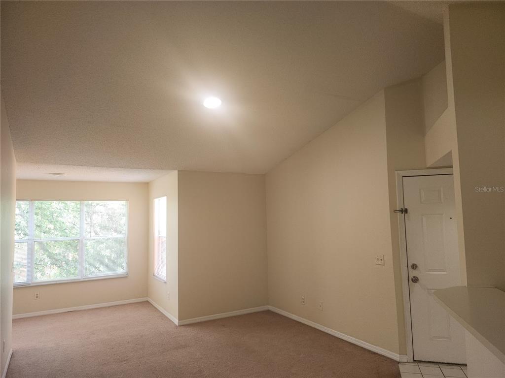 A living room with beige carpet, light-colored walls, a vaulted ceiling, and a white door — 4518 COMMANDER DRIVE UNIT 1934, ORLANDO, FL