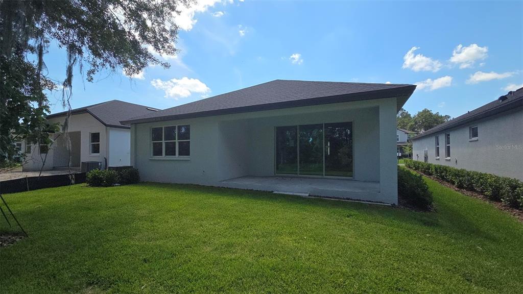 The backyard view shows a light-colored house with a covered patio and sliding glass doors — 19451 FOREST GARDEN COURT, BROOKSVILLE, FL