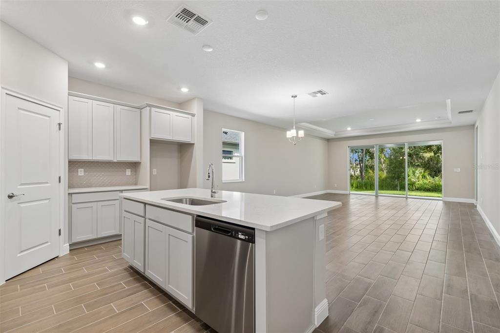A kitchen with light gray cabinets, a white island, and tile flooring overlooks an open living area — 19451 FOREST GARDEN COURT, BROOKSVILLE, FL