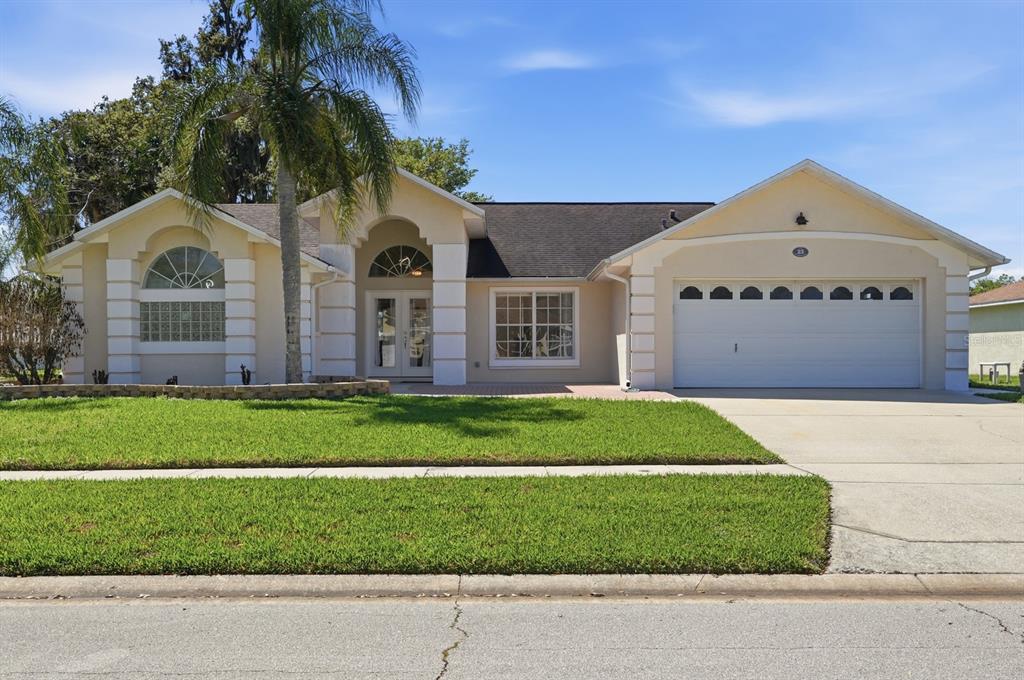 A single-story house with a beige stucco exterior, a palm tree, and a two-car garage — 23 OLD SUNBEAM DRIVE, SOUTH DAYTONA, FL