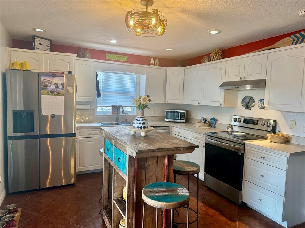 A kitchen features white cabinets, stainless steel appliances, and a rustic wooden island with stools — 107 DOUGLAS STREET, EDGEWATER, FL