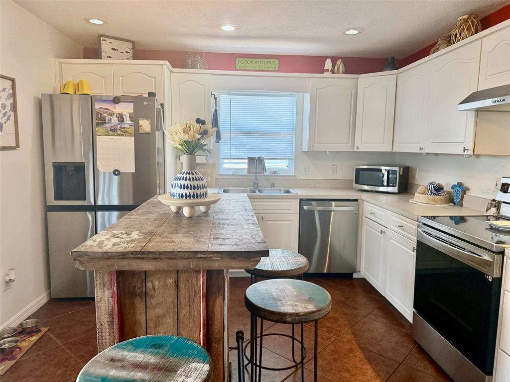 A kitchen features white cabinets, stainless steel appliances, a rustic wooden island, and tile flooring — 107 DOUGLAS STREET, EDGEWATER, FL