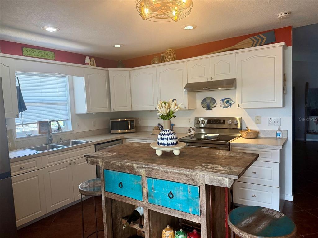 A kitchen features white cabinetry, a rustic wooden island with blue drawers, and tile flooring — 107 DOUGLAS STREET, EDGEWATER, FL
