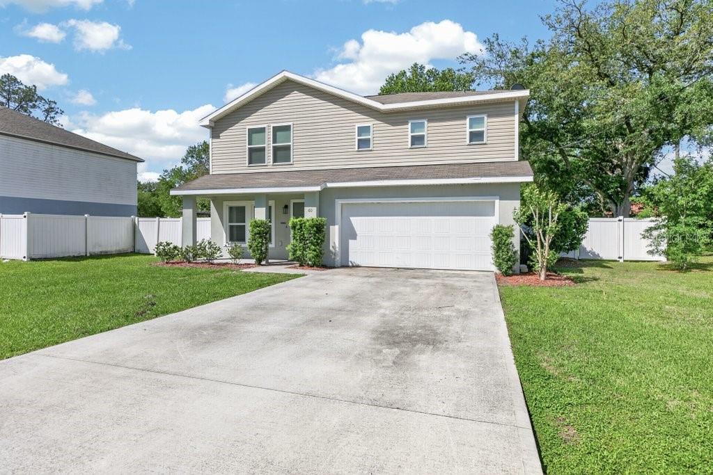 A two-story house with beige siding, a white garage door, and a concrete driveway — 60 PINE CREST LANE, PALM COAST, FL
