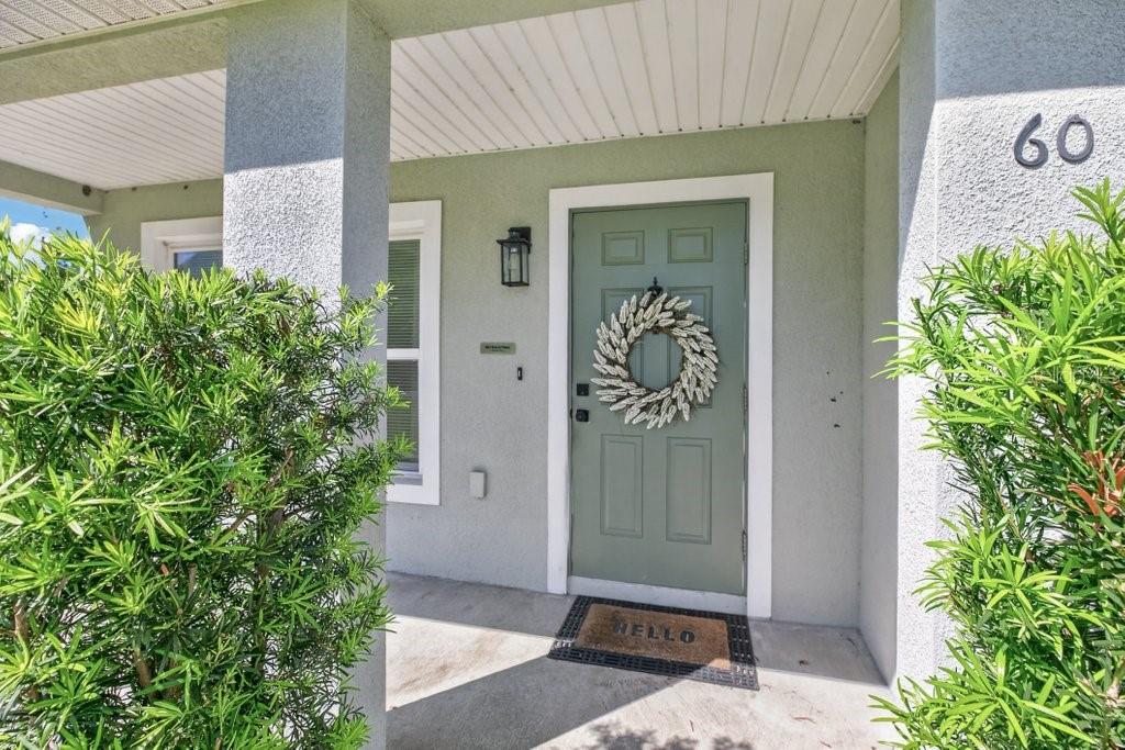 A sage green front door with a wreath and a hello doormat under a porch — 60 PINE CREST LANE, PALM COAST, FL