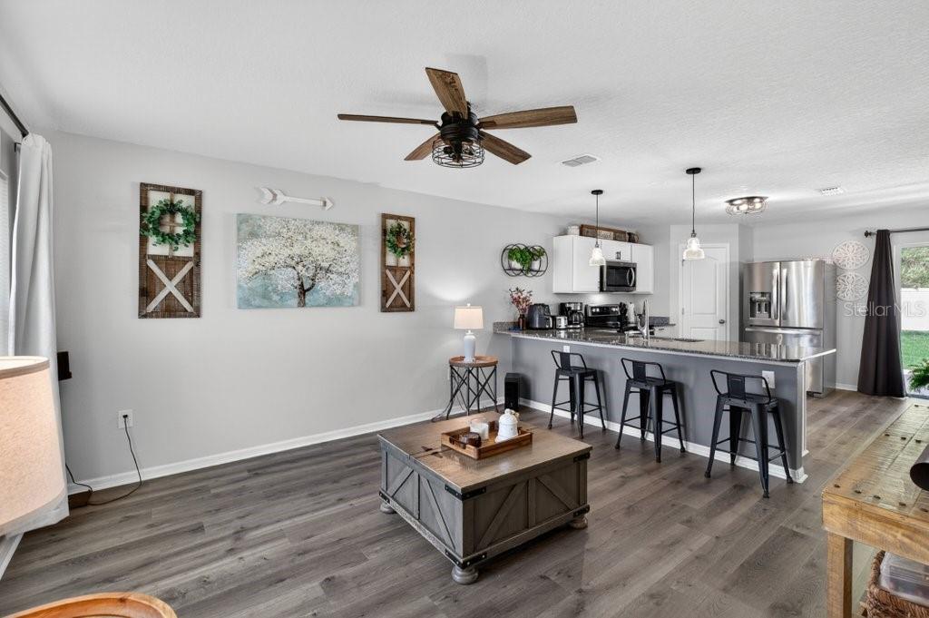 A living room with wood-look flooring, a coffee table, and an open kitchen with bar seating — 60 PINE CREST LANE, PALM COAST, FL