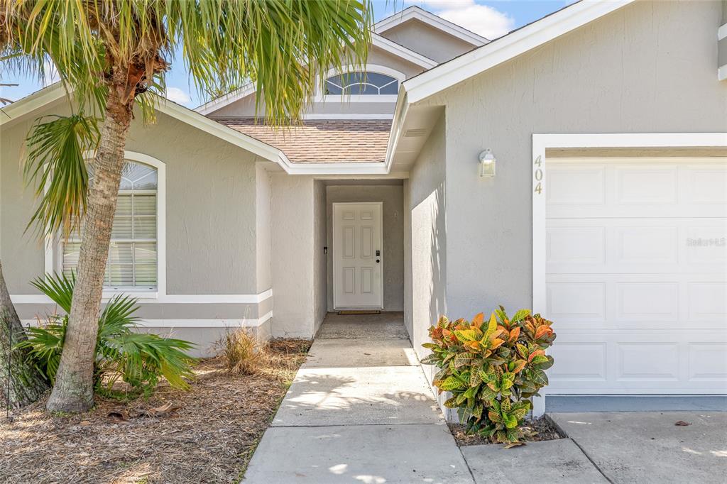 The exterior of a gray house features a front door, a garage, and a palm tree — 404 EMERALD COVE LOOP, LAKELAND, FL