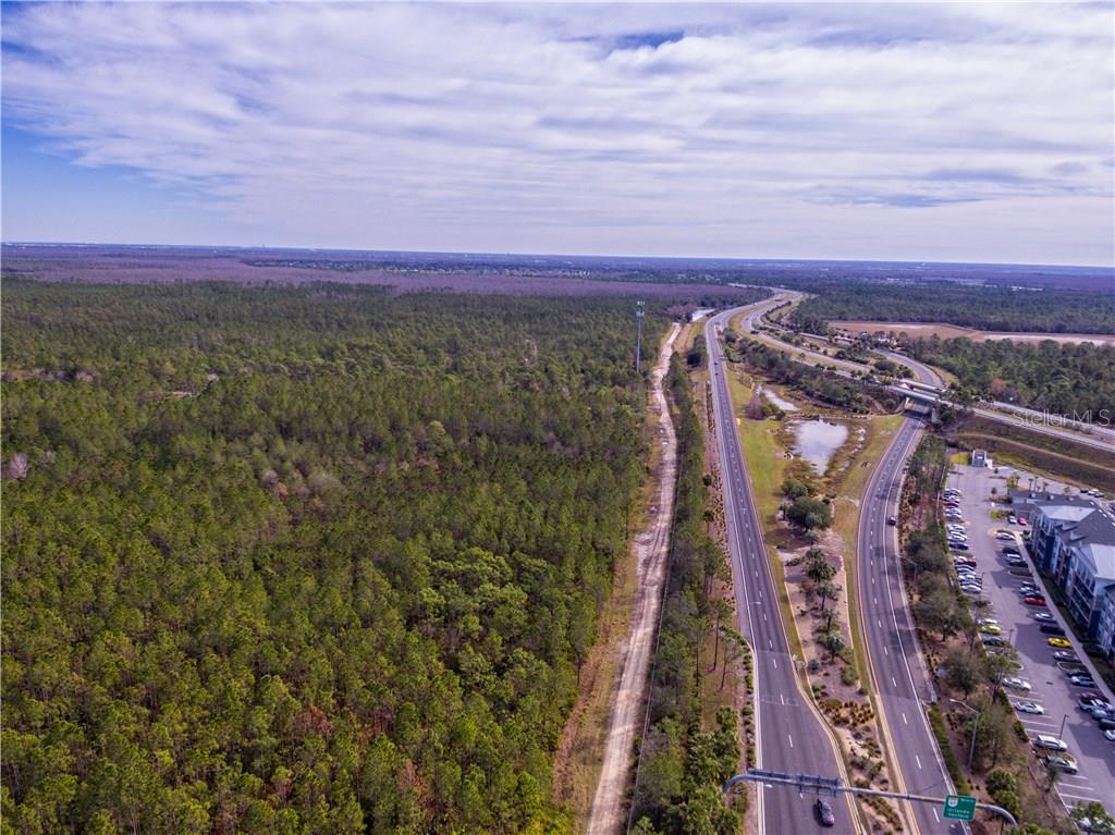 An aerial view shows a multi-lane highway running alongside a large, dense forest area — INTERNATIONAL DRIVE, ORLANDO, FL