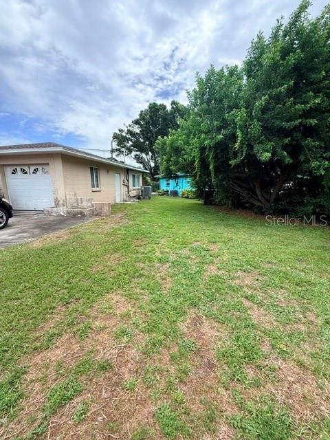 A grassy yard extends toward a tan house with a garage and a blue building — 830 55TH AVENUE S, ST PETERSBURG, FL