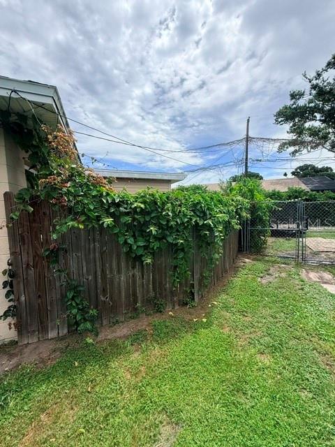 A wooden fence covered in climbing vines stands in a grassy backyard under a cloudy sky — 830 55TH AVENUE S, ST PETERSBURG, FL