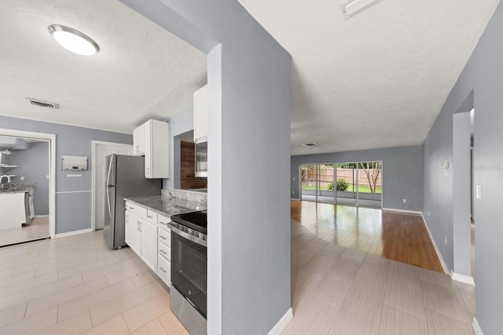 A kitchen with white cabinets and stainless steel appliances opens into a living area — 208 TALLEY DRIVE, PALM HARBOR, FL
