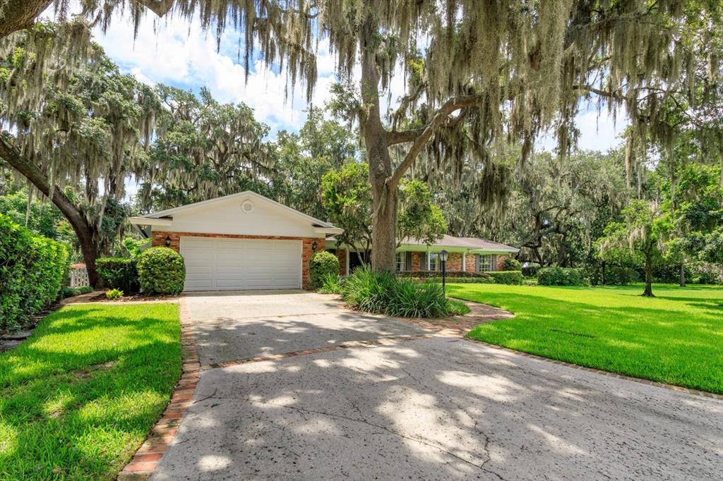 A single-story house with a white garage and brick accents sits under large mossy trees — 5019 GRAN LAC AVENUE, ORLANDO, FL