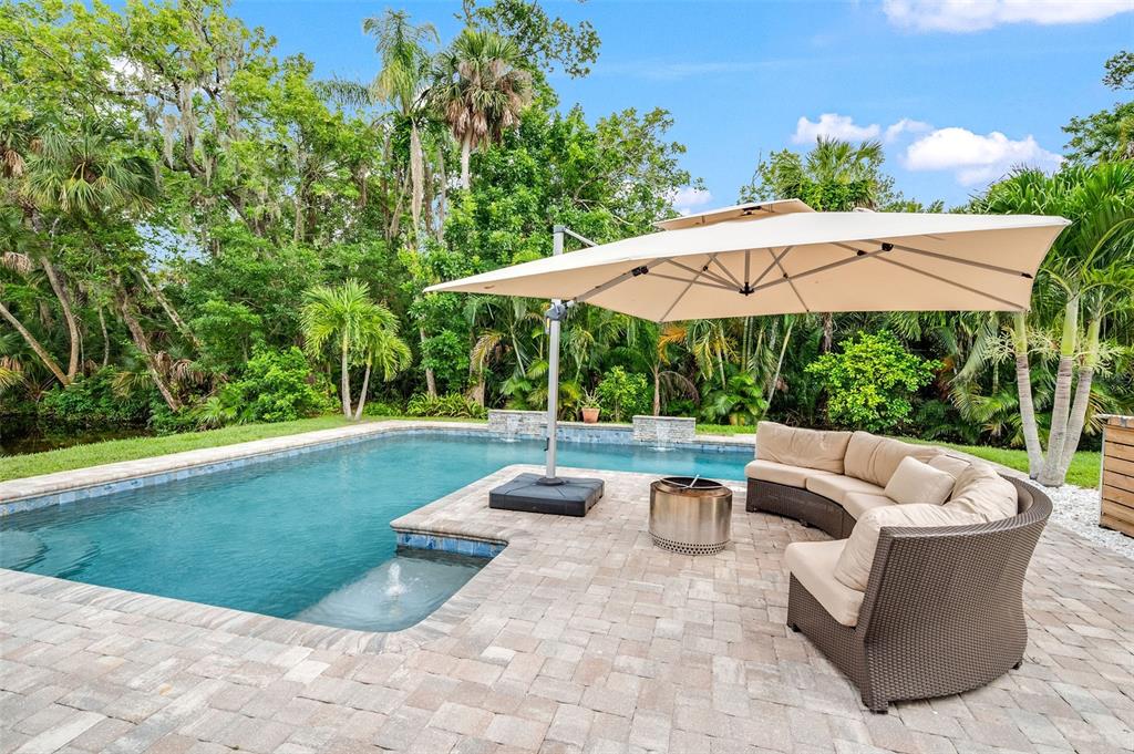 A swimming pool with a patio, fire pit, and outdoor umbrella in a lush backyard — 105 BRIARWOOD LANE, COCOA, FL